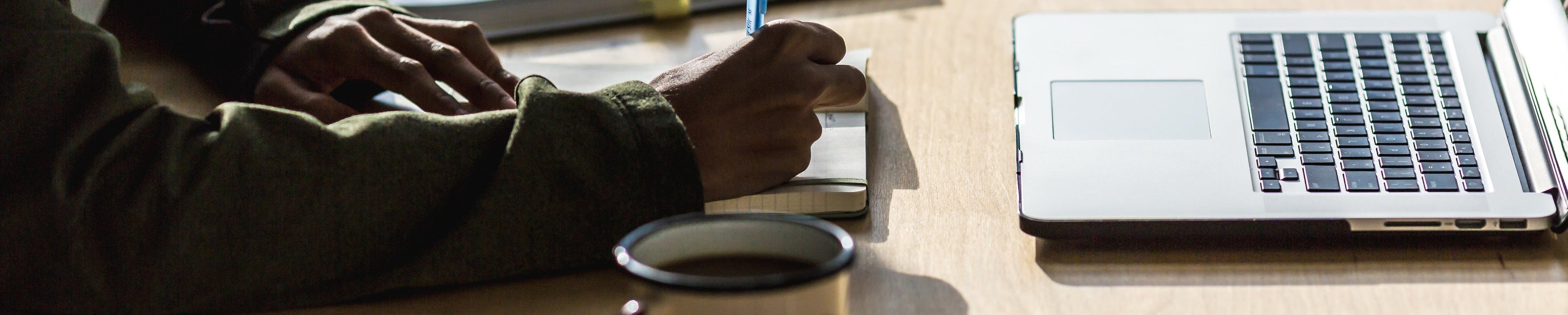Person sitting at a desk with a laptop, pen, and coffee cup.